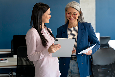 Two smiling women looking at notepad at work